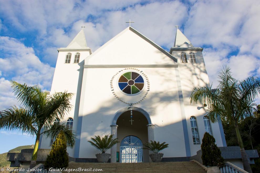 Imagem da fachada de uma igreja com um grande terço na frente pendurado na Pedra Azul.